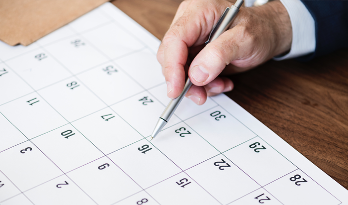 A white male's hand holding a pen and pointing to a company holiday date on the calendar. 