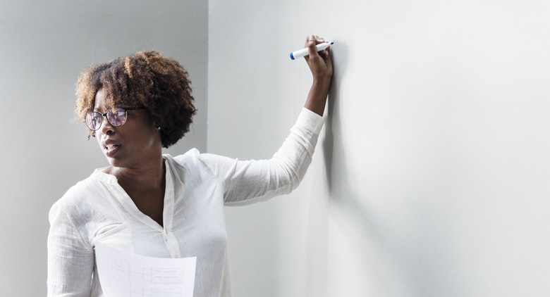 A black female HR manager writing development strategies on a wall to develop her employees. 