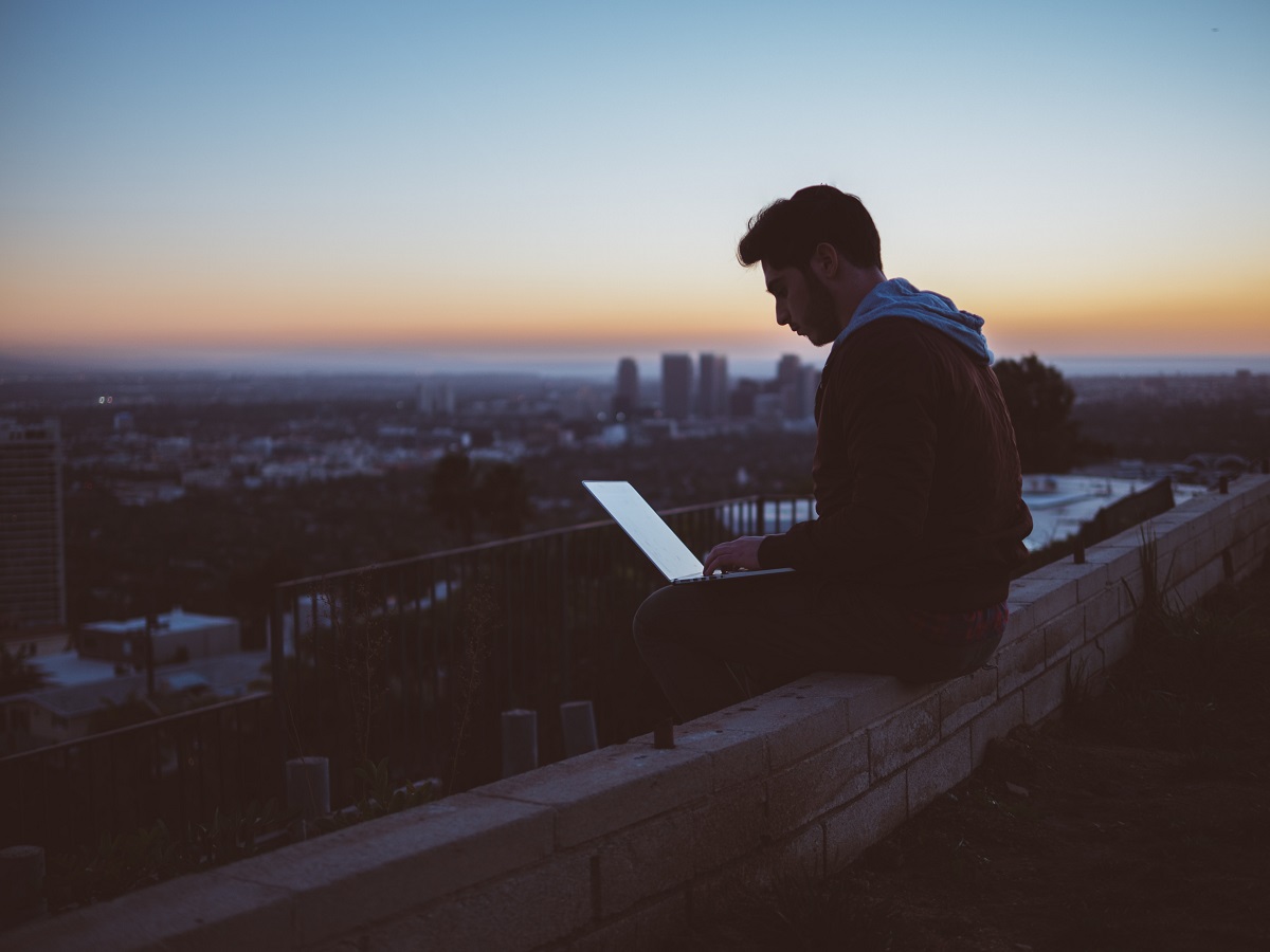 man sitting on ledge working on laptop