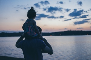 father with daughter on shoulders looking out at ocean